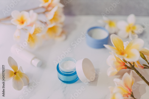group of skincare products including moisturiser scrub and hand cream pots on marble table with exotic frangipani flowers