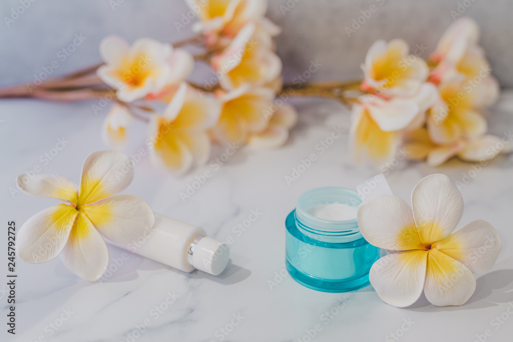 group of skincare products including moisturiser and hand cream pots on marble table with exotic frangipani flowers group of skincare products including moisturiser and hand cream pots on marble table with exotic frangipani flowers
