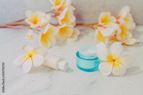 group of skincare products including moisturiser and hand cream pots on marble table with exotic frangipani flowers