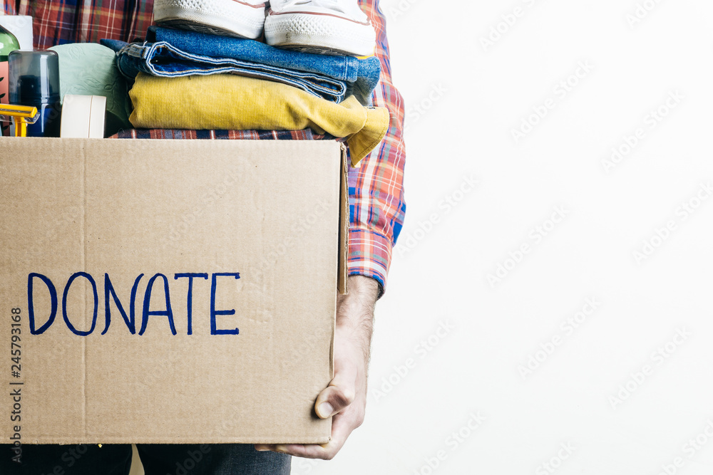 Fototapeta premium CLOTHES DONATION AND FOOD DONATION CONCEPT. A man holding a donation box with clothes, shoes and hygiene products. Copy space