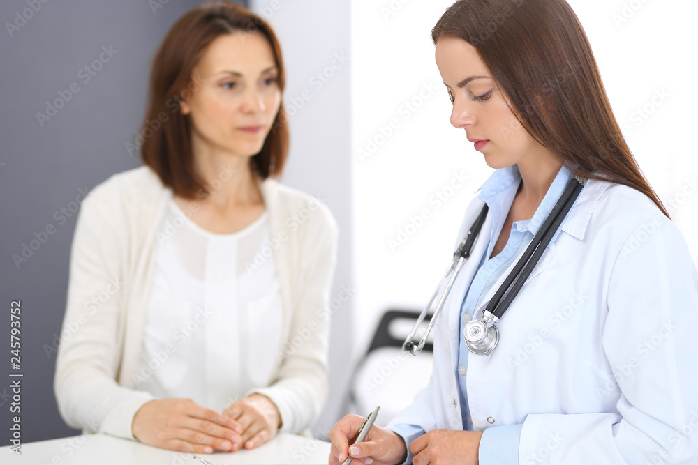 Doctor and patient discussing something while standing near reception desk in emergency hospital. Physician at work in clinic. Medicine and health care concept Doctor and patient discussing something while standing near reception desk in emergency hospital. Physician at work in clinic. Medicine and health care concept