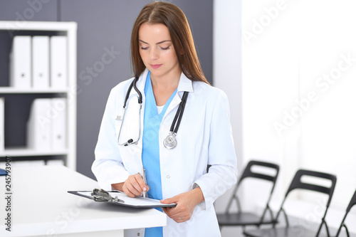 Doctor woman at work. Portrait of female physician filling up medical form while standing near reception desk at clinic or emergency hospital. Medicine and healthcare concept