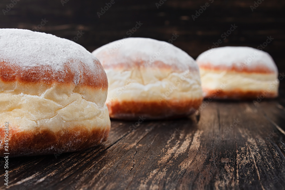 Freshly made doughnuts filled with jam and covered in powdered sugar on a rustic wooden table Freshly made doughnuts filled with jam and covered in powdered sugar on a rustic wooden table