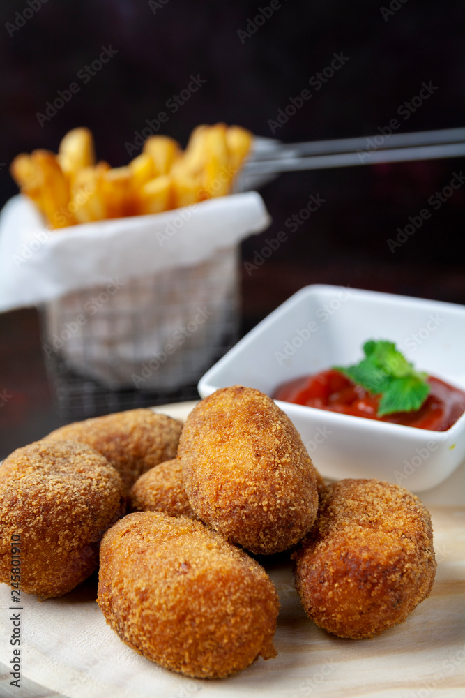 Croquettes on a wood plate with fried tomate and chips