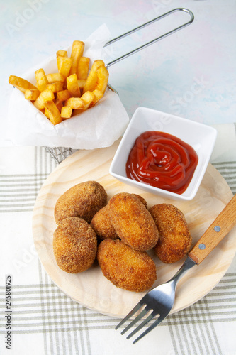 Croquettes on a wooden dish and chips, fried tomate and fork