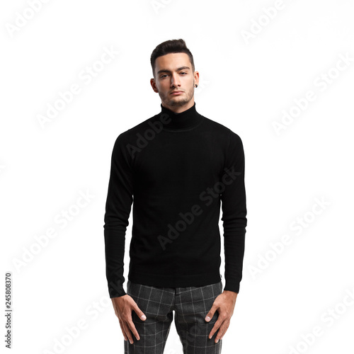 Young man dressed in black turtleneck and gray plaid pants stands on the white background