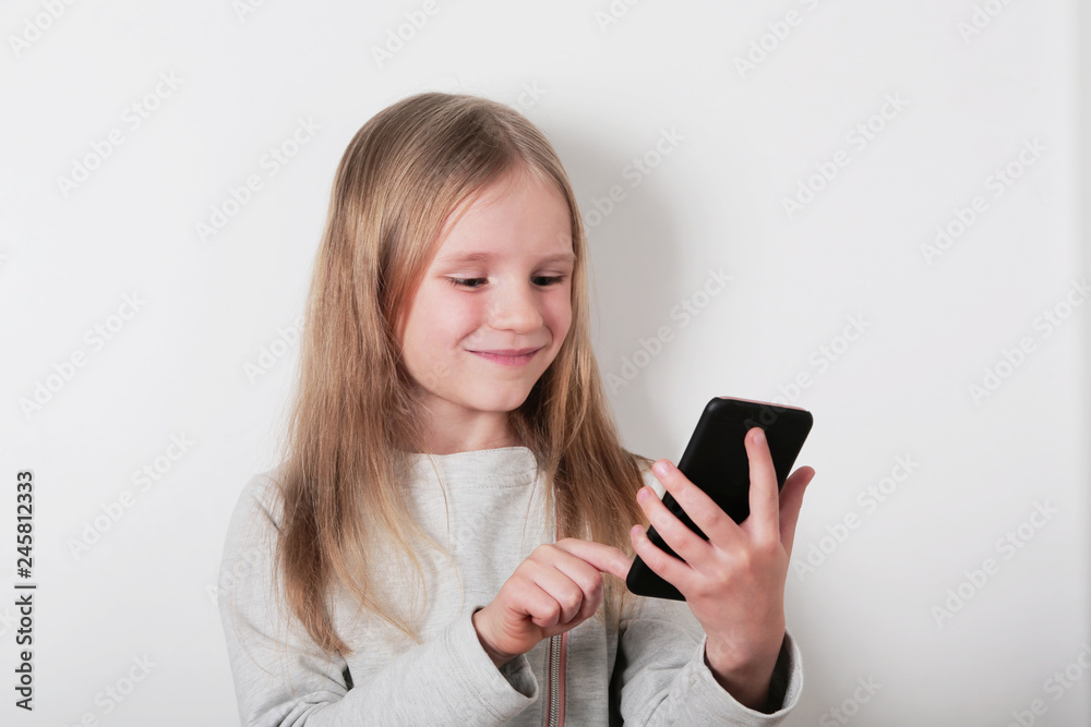 Portrait of a smiling little blonde girl looking at mobile phone , smartphone on white background Portrait of a smiling little blonde girl looking at mobile phone , smartphone on white background