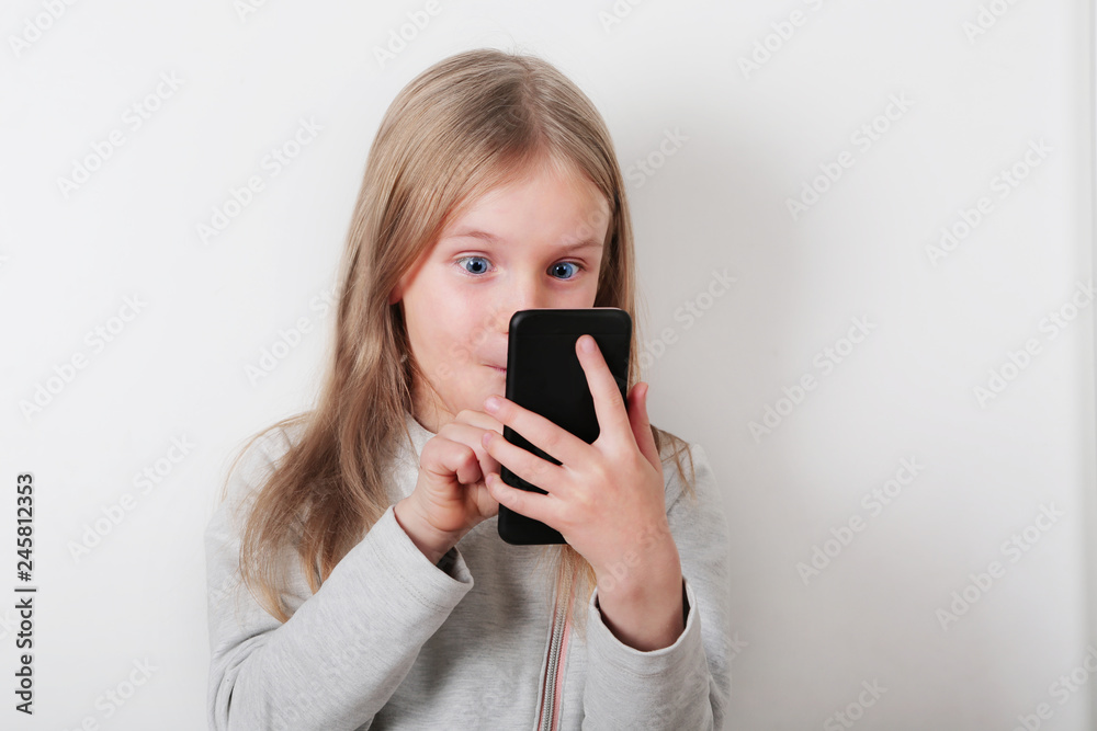 Portrait of a smiling little blonde girl looking at mobile phone , smartphone on white background Portrait of a smiling little blonde girl looking at mobile phone , smartphone on white background