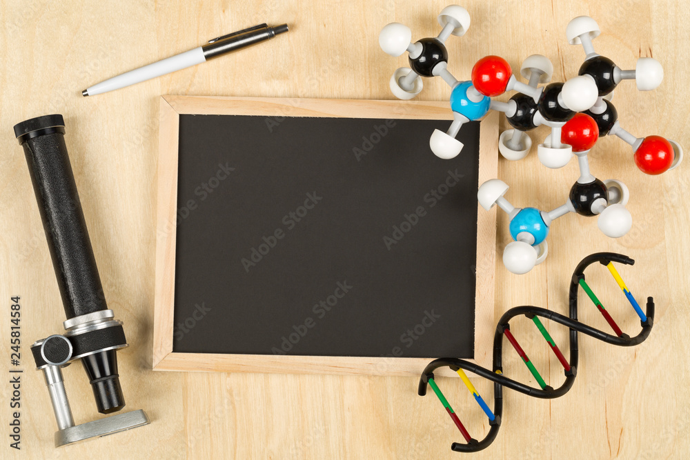 Blank, empty, black chalkboard with microscope, molecule model, pen and DNA model flat lay on brown wooden desk