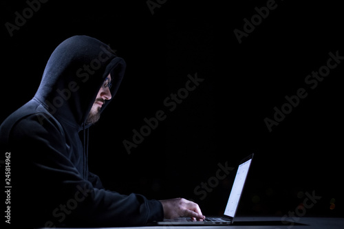hacker using laptop computer while working in dark office