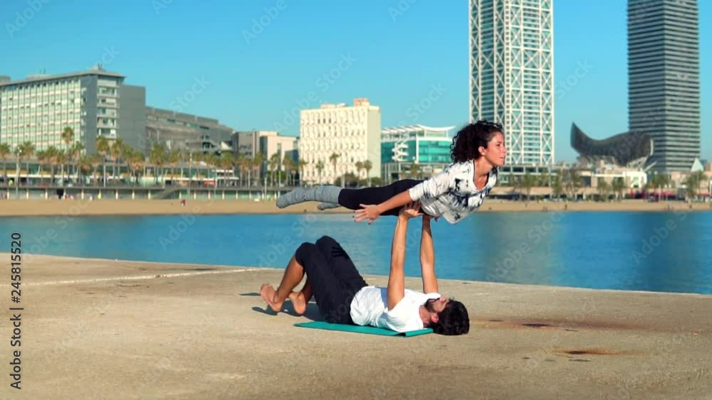 Beautiful couple practicing acro yoga in the morning outdoors near the sea. Balance and connection concept. slowmotion shot Beautiful couple practicing acro yoga in the morning outdoors near the sea. Balance and connection concept. slowmotion shot