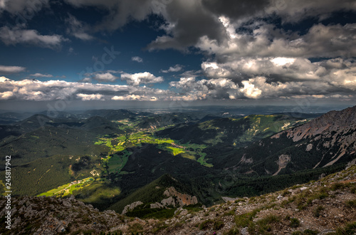 Scenic view with dark, blue, cloudy, sky from Rax plateau, Schneeberg massif, on valley with Puchberg village, rubble fields and green forest, Raxalpe, Alps, Lower Austria photo