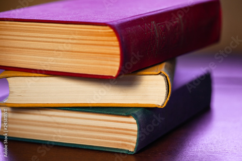 close-up old big books with red  yellow and green covers are lying on a wooden table in a purple light