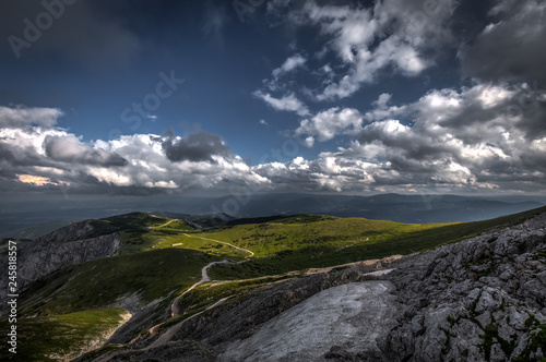 Small patch of snow in the summer in the middle of grassy meadow in rax plateau, near route Dambocksteig from Schneeberg, highest peak Kosterwappen in the cloudy sunset, Raxalpe, Lower Austria photo