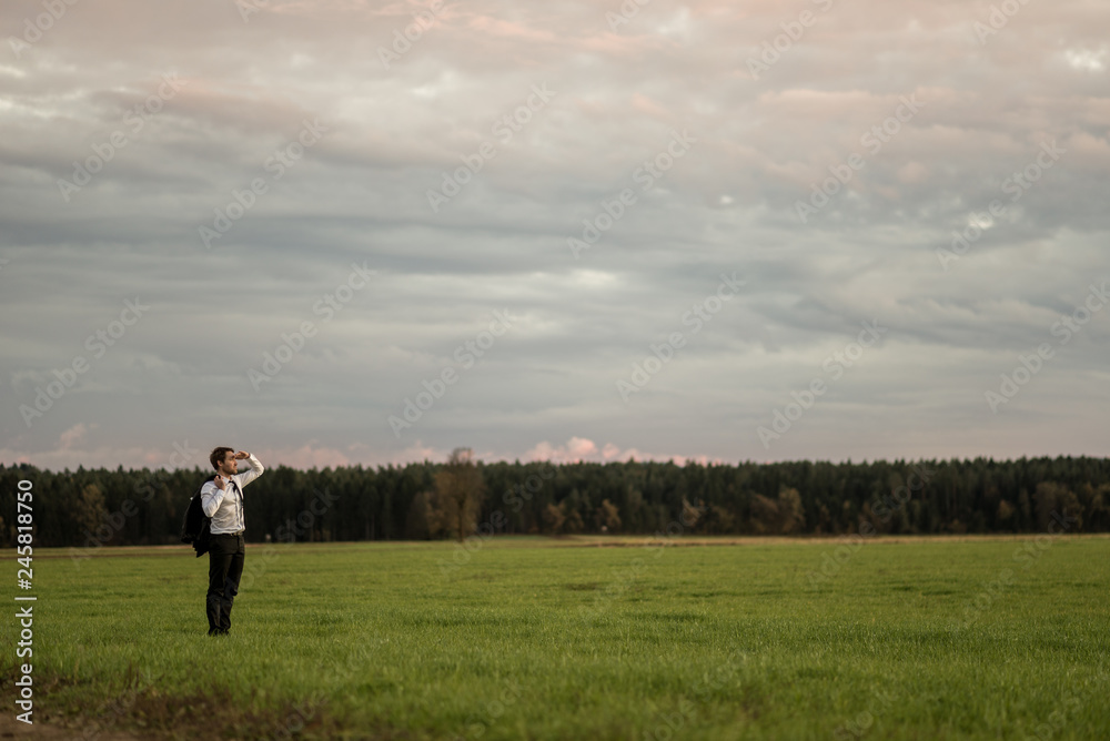 Young businessman standing in green meadow looking in to a distance