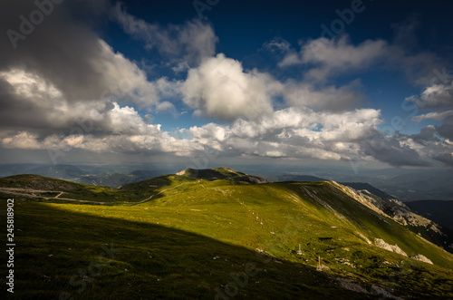 Green grassy rax plateau with big patch of shade and dramatic, cloudy, dark blue sky near Klosterwappen, highest peak of Schneeberg on route Dambocksteig, Raxalpe, Lower Austria photo