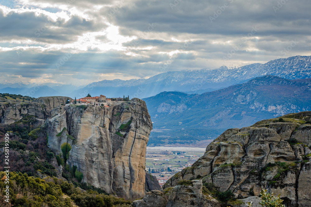 Agios Stephanos or Saint Stephen monastery situated on the huge rock with sunset rays and mountains in the background, Meteors, Trikala, Thessaly, Greece