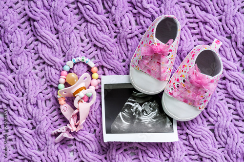 Blue booties next to baby photos with ultrasound at 20 weeks of pregnancy. The concept of awaiting baby boy, pregnancy. A son. Selective focus.