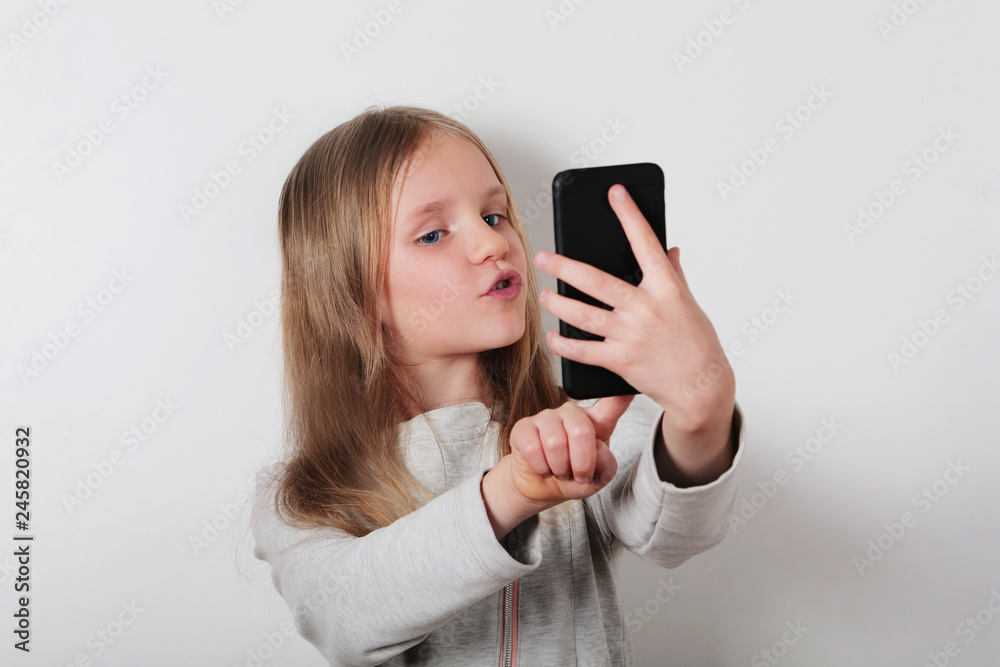 Portrait of a cheerful little girl taking a selfie with mobile phone , smartphone on white background Portrait of a cheerful little girl taking a selfie with mobile phone , smartphone on white background