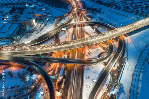 Aerial view of road in the modern city at night in winter. Top view of traffic in highway junction with illumination. Elevated road and interchange overpass. Busy intersection. Expressway and motorway