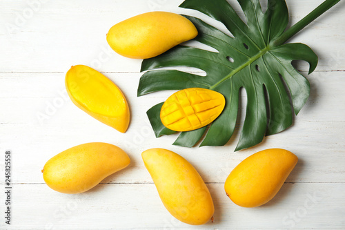 Flat lay composition with mango and tropical leaf on wooden background