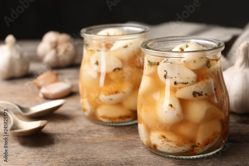 Preserved garlic in glass jars on wooden table, closeup. Space for text