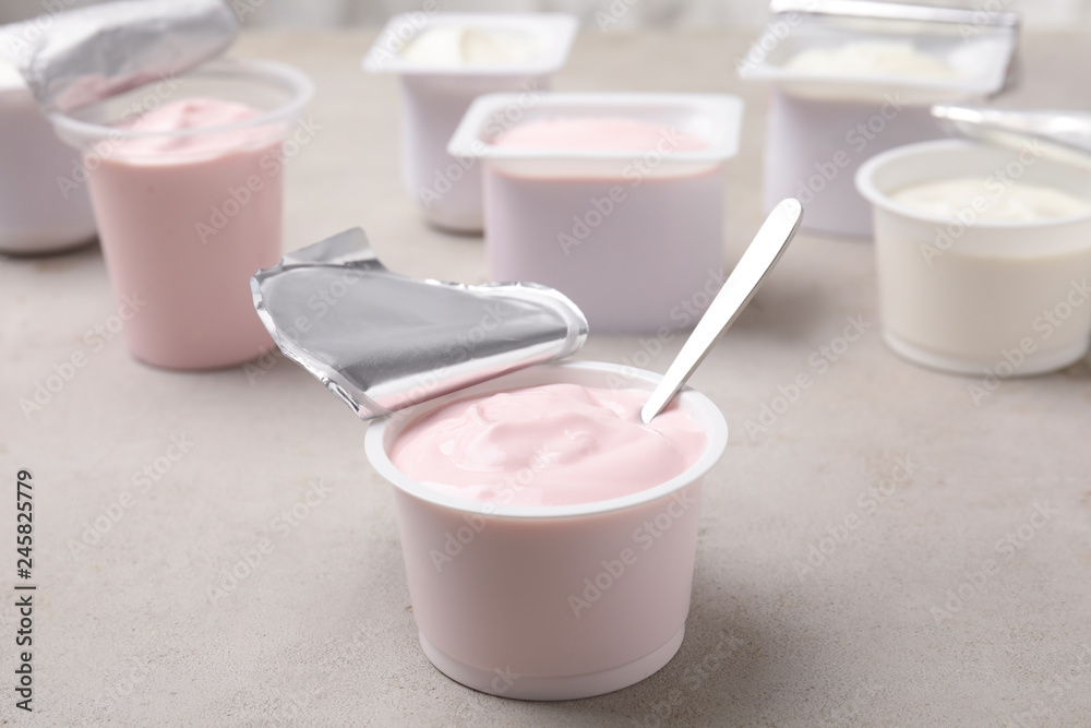 Plastic cup with fresh yogurt and spoon on grey table Plastic cup with fresh yogurt and spoon on grey table