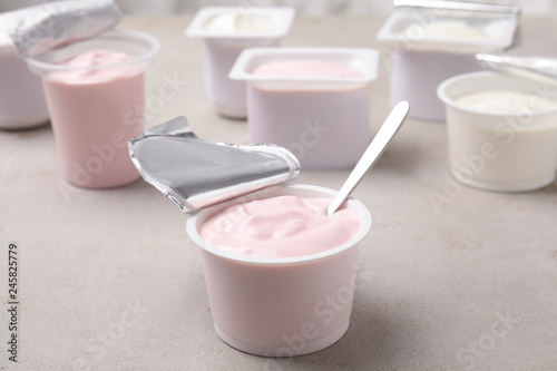Plastic cup with fresh yogurt and spoon on grey table
