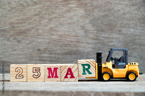 Toy forklift hold block R to complete word 25mar on wood background (Concept for calendar date 25 in month March) photo