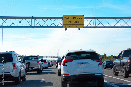 Toll Plaza 1/2 MILE yellow sign on overhead metal tri-chord truss with toll booths in the far distance and cars in traffic jam