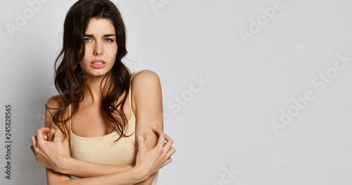 Young woman allergy scratching her arms hands with fingers on gray