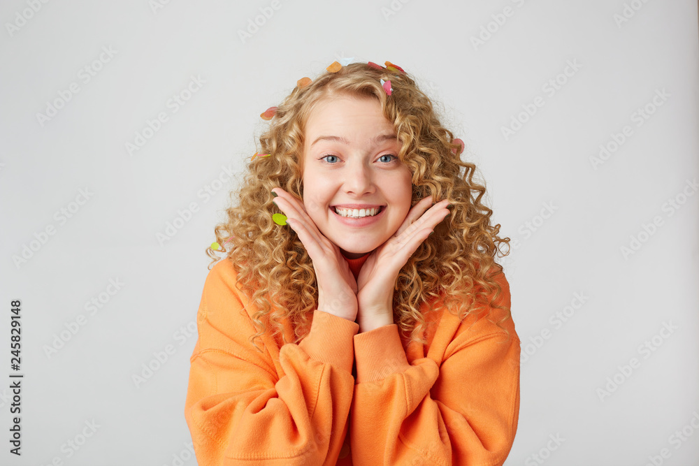 Portrait of lovely tender nice blonde looks excited, surprised, keeps palms near face, dressed in oversized orange sweater, isolated on a white background Portrait of lovely tender nice blonde looks excited, surprised, keeps palms near face, dressed in oversized orange sweater, isolated on a white background