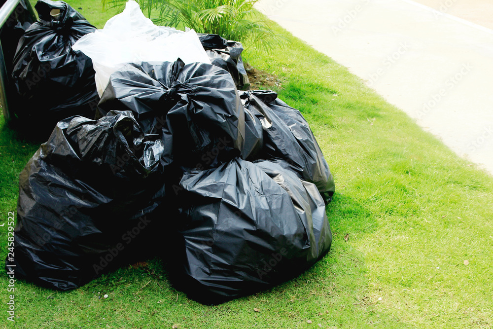 The black plastic bag is filled with garbage on the lawn. The black plastic bag is filled with garbage on the lawn.