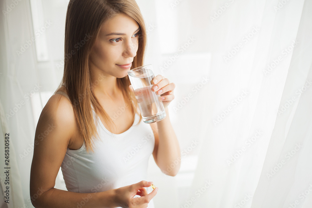 Happy smiling positive woman eating the pill and holding the glass of water in the hand, in her home Happy smiling positive woman eating the pill and holding the glass of water in the hand, in her home