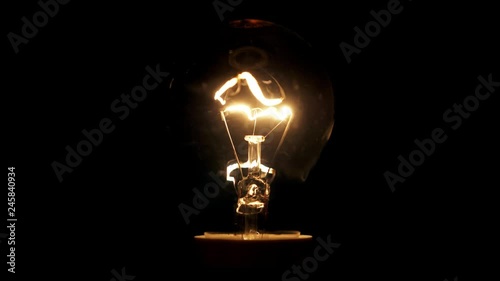 In the dark light comes on and goes out. Incandescent lamp shines. Yellow incandescent bulb, close-up, macro.