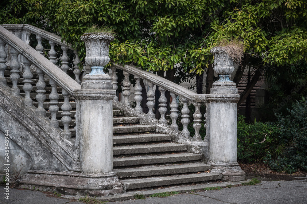 Ancient staircase with stone balusters against the background of green vegetation.