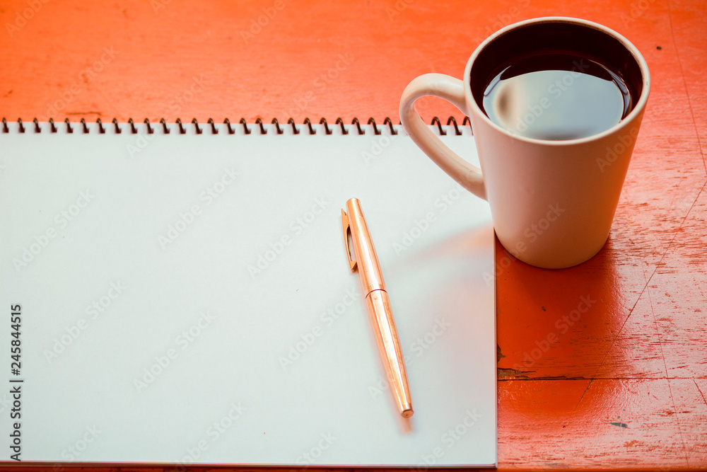 libreta de notas de papel blanco sobre un escritorio de oficina con un  lapicero y junto a una taza de café blanca / ambiente de trabajo en oficina  / trabajando Stock Photo