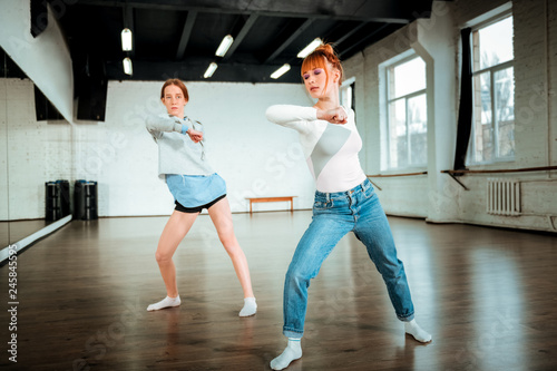 Beautiful red-haired professional dancer in blue jeans and her student moving energetically