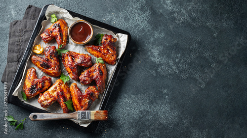 Roasted chicken wings in barbecue sauce with sesame seeds and parsley in a baking tray on a dark table. Top view with copy space. Tasty snack for beer on a dark background. Flat lay
