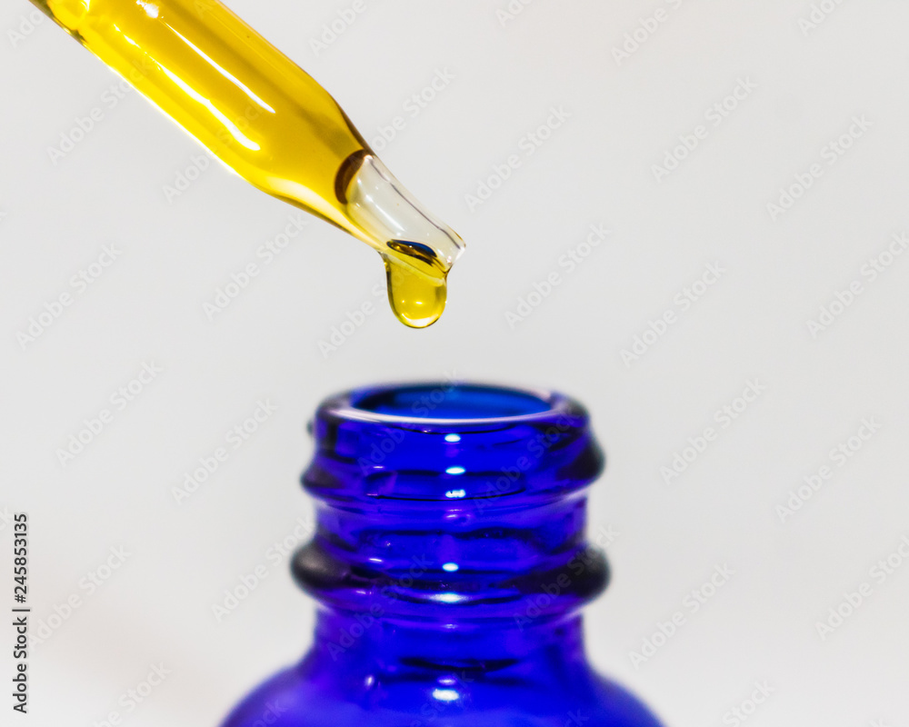 CBD oil tincture dropping into blue bottle up close isolated on white background CBD oil tincture dropping into blue bottle up close isolated on white background