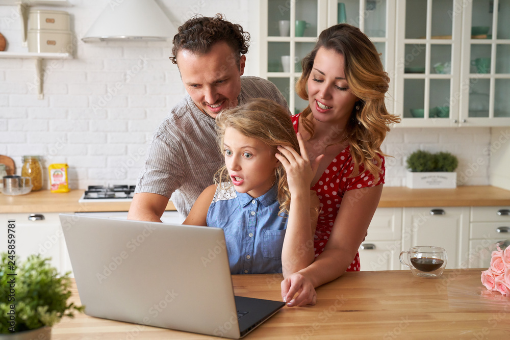 Young happy family surfing internet with laptop on table at kitchen Young happy family surfing internet with laptop on table at kitchen