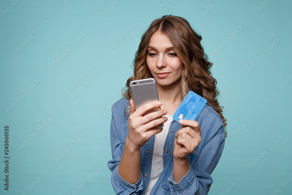 Image of excited young lady isolated over blue background using mobile phone holding credit card. Image of excited young lady isolated over blue background using mobile phone holding credit card.