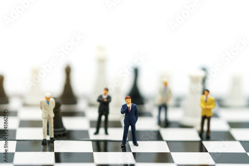 Miniature people: Businessman handshake to business success on chessboard. Commitment, agreement, investment and partnership concept