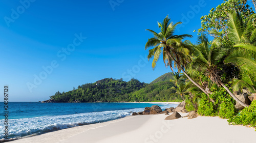 Panorama of sandy beach with beautiful rocks, coco palms and turquoise sea on Seychelles island. 