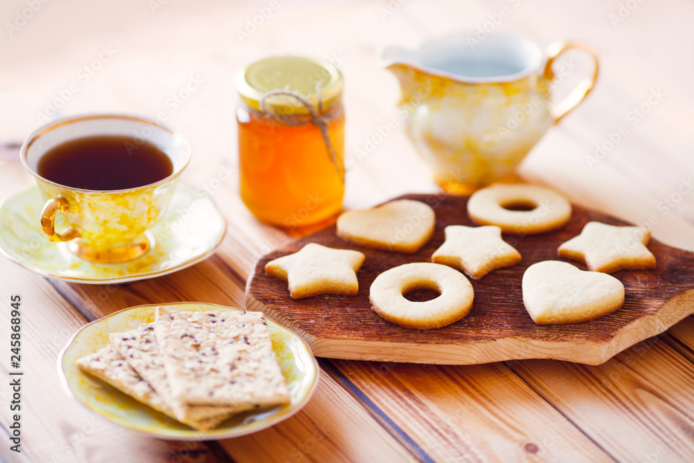 Beautiful set of homemade cookies stars and hearts on the brown decorative board, vintage cup of tea and honey. Sunny morning. Food, break, cooking, lifestyle concept. Top view. Close up. Beautiful set of homemade cookies stars and hearts on the brown decorative board, vintage cup of tea and honey. Sunny morning. Food, break, cooking, lifestyle concept. Top view. Close up.