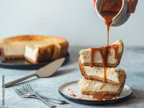 Caramel pouring on stack of three cheesekace pieces. Cheesecake with caramel on gray cement background. Copy space for text. photo