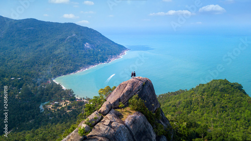 Man and woman standing on cliff's edge and looking into a sand beach of koh Phangan island,Thailand photo