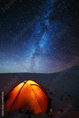 A charming night in the Carpathian Mountains with a tourist in a red tent and a Milky way with millions of stars in the sky.