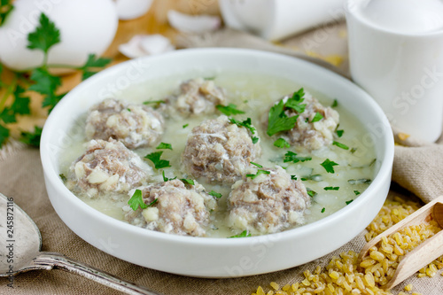 Armenian white sour soup on chicken broth with meatballs, bulgur and green parsley