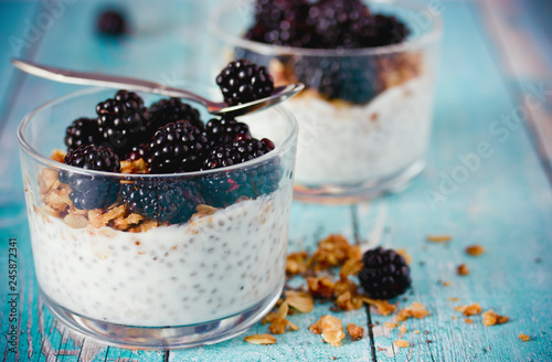Chia pudding with granola and fresh blackberry in glass on blue wooden background, healthy food idea